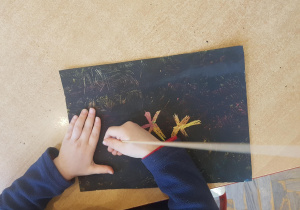 Dzieci pracują przy stoliku. Za pomocą wykałaczki występują we wcześniej przygotowanym kartonie kolorowe wzory - fajerwerki.